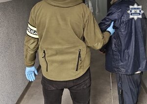 Na zdjęciu nieumundurowany policjant prowadzi zatrzymanego