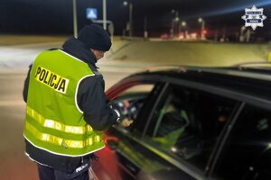 policjant sprawdzający trzeźwość kierowcy stojący przy samochodzie.