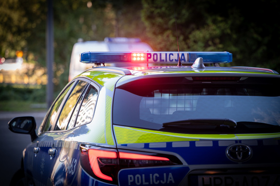 zdjęcie radiowozu z włączonymi sygnałami błyskowymi, zrobione od tyłu.