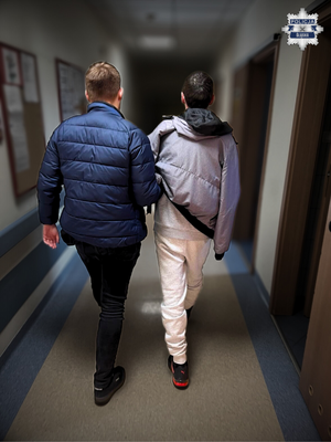 Zatrzymany prowadzony przez policjanta po korytarzu komendy.