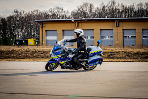 Jadący po kole policjant na służbowym motocyklu.