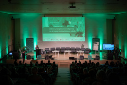 Zdjęcie przedstawia prelegentkę na mównicy - ujęcie z końca sali