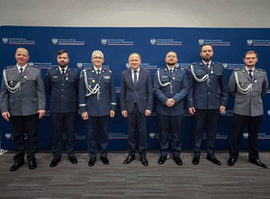 Na zdjęciu na ściance Ministerstwa Spraw Wewnętrznych i Administracji widzimy Sekretarza Stanu wspomnianego ministerstwa wraz z Komendantem Wojewódzkim Komendy Wojewódzkiej w Katowicach i pięcioma uhonorowanymi policjantami.