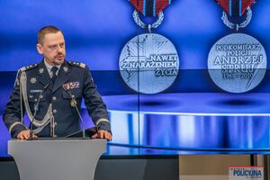 Na tle medali wyświetlonych na ścianie widzimy przemawiającego Komendanta Głównego Policji.