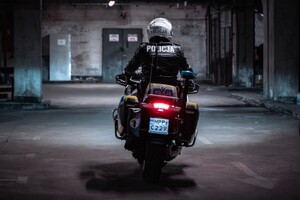 Widzimy policjanta na motocyklu, motocykl ustawiony tyłem do nas. Zdjęcie wykonane na parkingu podziemnym, tworząc mroczną scenerie