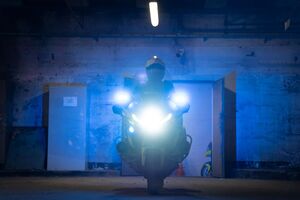 Widzimy policjanta na motocyklu, motocykl ustawiony przodem do nas z włączonymi światłami tworząc ciekawy nastrój