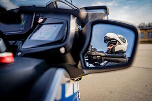 Zbliżenie na lusterko motocykla, na którym widać odbicie policjanta w kasku motocyklowym