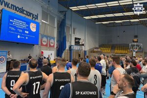 Na hali sportowej stoją koszykarze w strojach sportowych