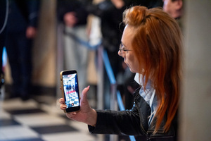 na zdjęciu kobieta trzyma telefon w ręce w którym na ekranie wyświetla się ślubowanie policjantów