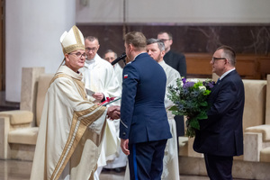 zdjęcie przedstawia funkcjonariusza policji ściskającego rękę duchownemu w kościele
