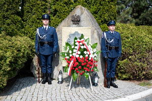 na zdjęciu pomnik przy którym wystawiony jest wieniec z czerwonych kwiatów, przy pomniku pełniący wartę funkcjonariusze policji