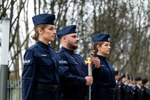 na zdjęciu funkcjonariusze Policji, policjant pośrodku trzyma zapaloną świecę