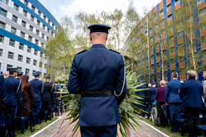 na zdjęciu funkcjonariusz policji trzymający wieniec, w tle Komenda Wojewódzka Policji w Katowicach