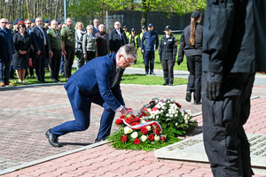 Mężczyzna w garniturze składa kwiaty pod pomnikiem
