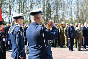 Policjanci z orkiestry, jeden gra na trąbce, w tle w szeregach stoją przedstawiciele służb