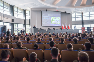 Policjant stoi przy mównicy na auli, na krzesłach siedzą uczestnicy konferencji