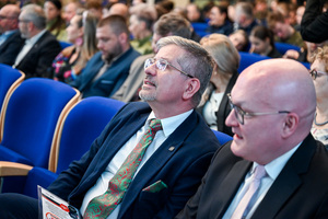 Uczestnicy konferencji i uczniowie siedzą na krzesłach w auli