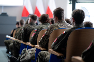 Uczestnicy konferencji i uczniowie siedzą na krzesłach w auli