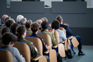 Uczestnicy konferencji i uczniowie siedzą na krzesłach w auli