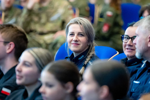 Uczestnicy konferencji i uczniowie siedzą na krzesłach w auli