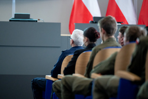 Uczestnicy konferencji i uczniowie siedzą na krzesłach w auli