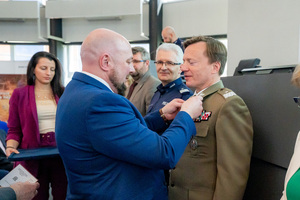 Mężczyzna w garniturze przypina medal żołnierzowi
