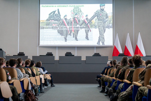 Uczestnicy konferencji i uczniowie siedzą na krzesłach w auli, oglądają prezentację multimedialną