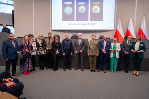 Uczestnicy konferencji, którzy zostali odznaczeni medalami, policjant, żołnierz, kobiety i mężczyźni stoją w auli