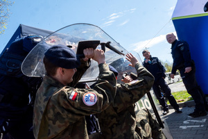 Policyjne stoisko profilaktyczne, uczniowie klas mundurowych, policjanci, uczniowie trzymają tarcze