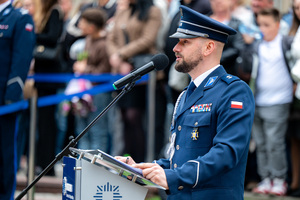 Policyjny lektor w mundurze galowym stoi przy mikrofonie