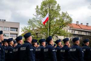 Policjanci w mundurach ćwiczebnych stoją w szeregu przy maszcie, na który jest wciągnięta flaga Polski