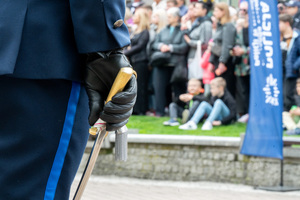 Fragment ręki policjanta, w której trzyma szablę, w tle osoby w ubraniach cywilnych