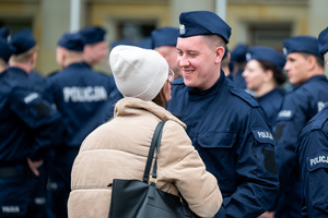Policjant w mundurze ćwiczebnym stoi przy kobiecie, w tle inni policjanci w mundurach ćwiczebnych