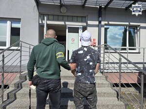 nieumundurowany policjant z opaską odblaskową na ręce z napisem policja, który prowadzi osobę