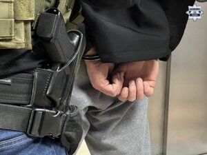 fragment kabury na pasie policyjnym wraz z bronią służbową i dłonie w kajdankach