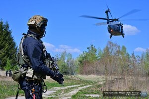Zdjęcie przedstawia policjanta a w tle śmigłowiec Black Hawk