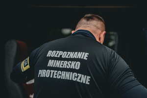 zdjęcie przedstawia policjanta z opaską na ramieniu policja
