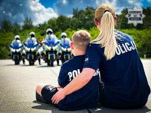 Zdjęcie przedstawia siedzącą tyłem policjantkę w mundurze wraz z dzieckiem.