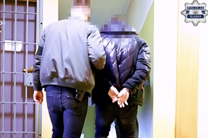 Zdjęcie przedstawiające policjanta stojącego tyłem wraz z osobą zatrzymaną.