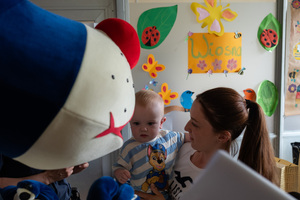 kobieta z dzieckiem na rękach obok policyjnej maskotki