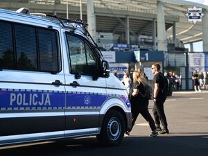Na zdjęciu widoczny jest radiowóz przed stadionem. W tle znajdują się przechodzący ludzie.