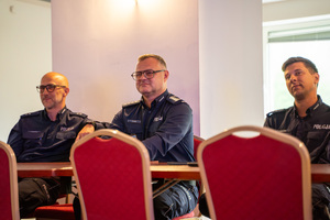 Na zdjęciu widocznych jest trzech siedzących, umundurowanych policjantów.