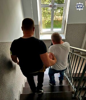 Na zdjęciu widoczny jest policjant doprowadzjący zatrzymanego mężczyznę