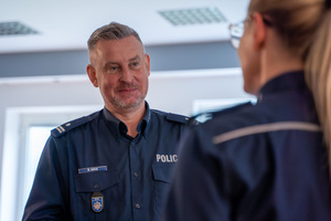Na zdjęciu widoczny jest Rzecznik Prasowy Komendanta Głównego Policji wraz z odwróconą plecami do zdjęcia Rzecznik Prasową Komendy Wojewódzkiej Policji w Katowicach.