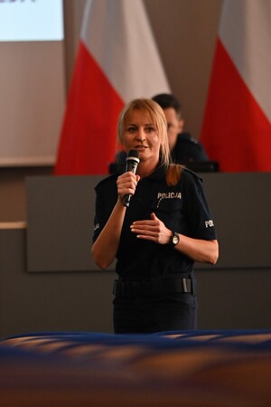 Na zdjęciu widoczna jest umundurowana policjantka z mikrofonem w ręku