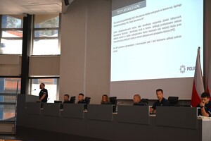 Zdjęcie przedstawia prowadzących szkolenie policjantów, w których tle znajduje się prezentacja z treścią szkolenia