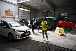 Na zdjęciu widoczny jest policjant wraz z uczestnikiem turnieju. Osoby znajdują się na hali, gdzie są pojazdy mechaniczne.