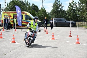 Na zdjęciu widoczny jest motocykl poruszający się po wyznaczonej trasie. W tle widoczni są policjanci oraz uczestnicy.