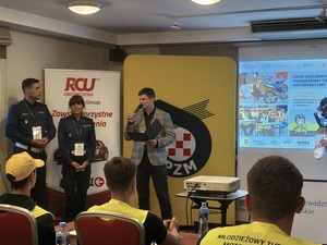 Na zdjęciu widać dwóch policjantów oraz organizatora mówiącego do mikrofonu.