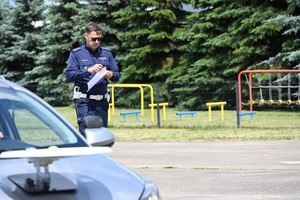 Na zdjęciu widoczny jest policjant pośrodku toru. Na pierwszym planie widoczny jest samochód osobowy.